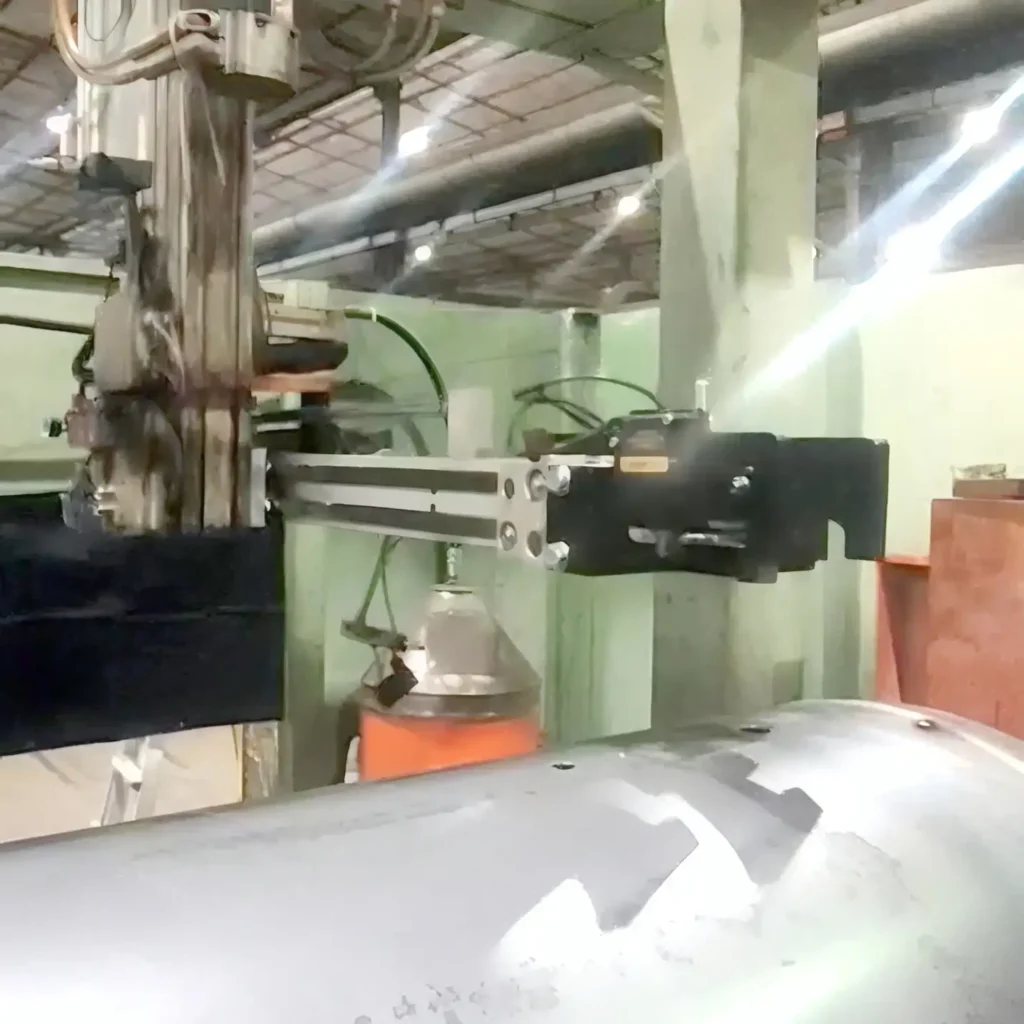 Industrial manufacturing setup with a robotic arm mounted on a linear slide attached to a green column, handling a metal workpiece in a factory.